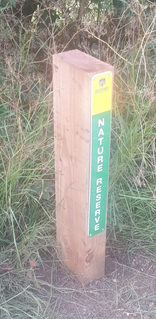 A post on the roadside verge with a sign reading Bedford Borough Council Nature Reserve